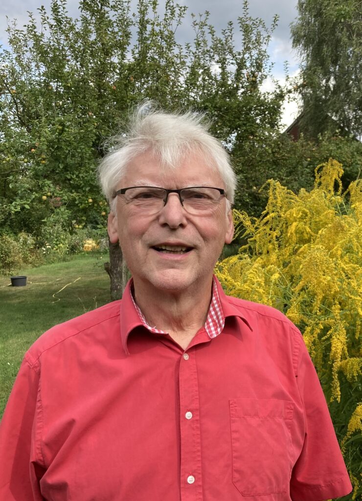 Porträtfoto von Gottfried Mahlke mit Brille und rotem Hemd in einem Garten.